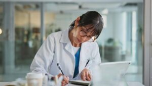 Médica escrevendo em caderno em consultório moderno