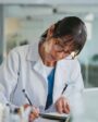 Médica escrevendo em caderno em consultório moderno