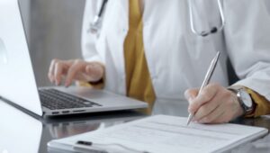 Médico digitando em laptop e anotando em papel