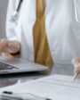 Médico digitando em laptop e anotando em papel