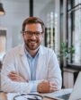 Médico sorridente em consultório moderno com laptop